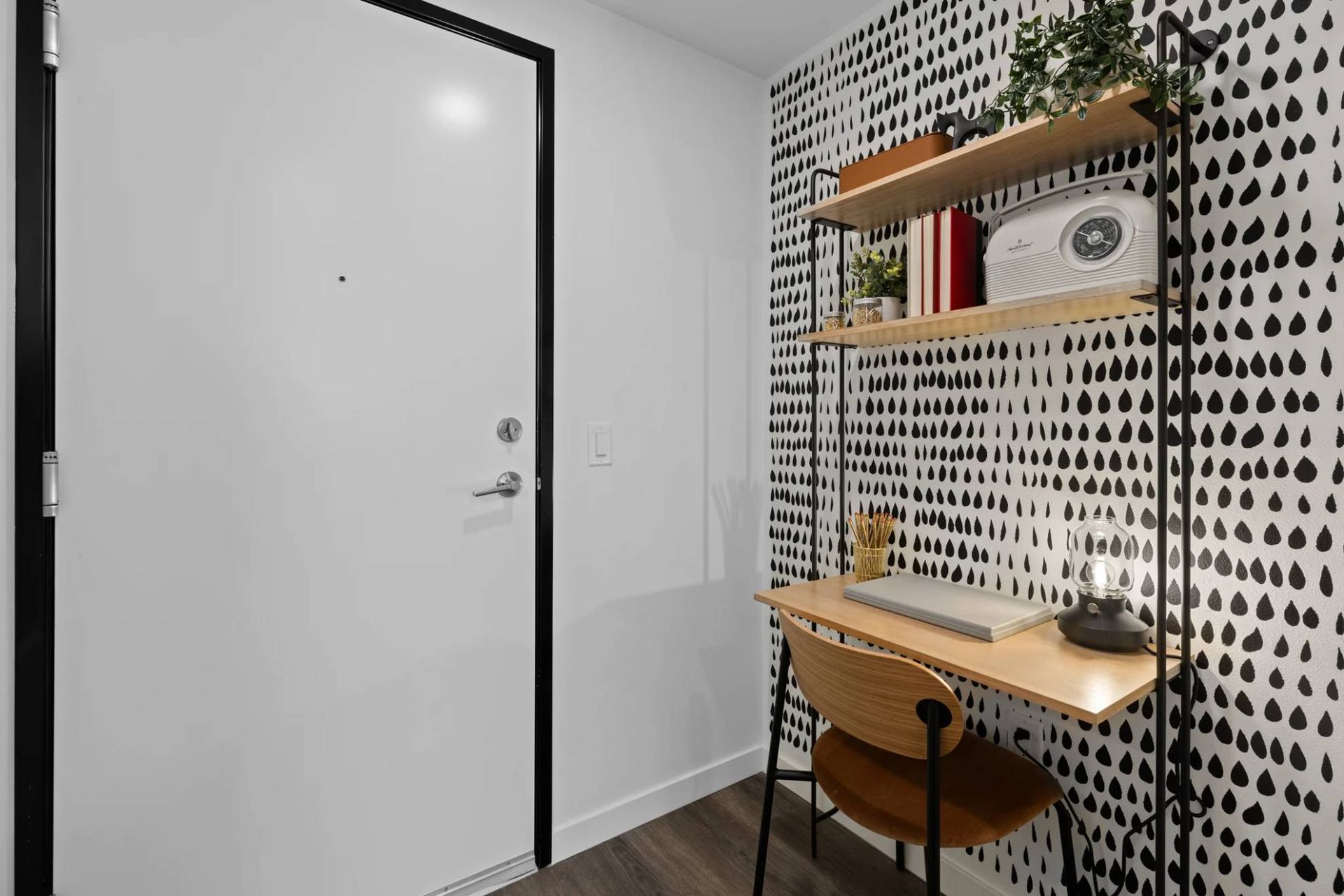 Corner apartment desk setup with a light wood desk, black metal shelving, and polka-dot wallpaper at Zinnia Apartments in Shoreline, WA.