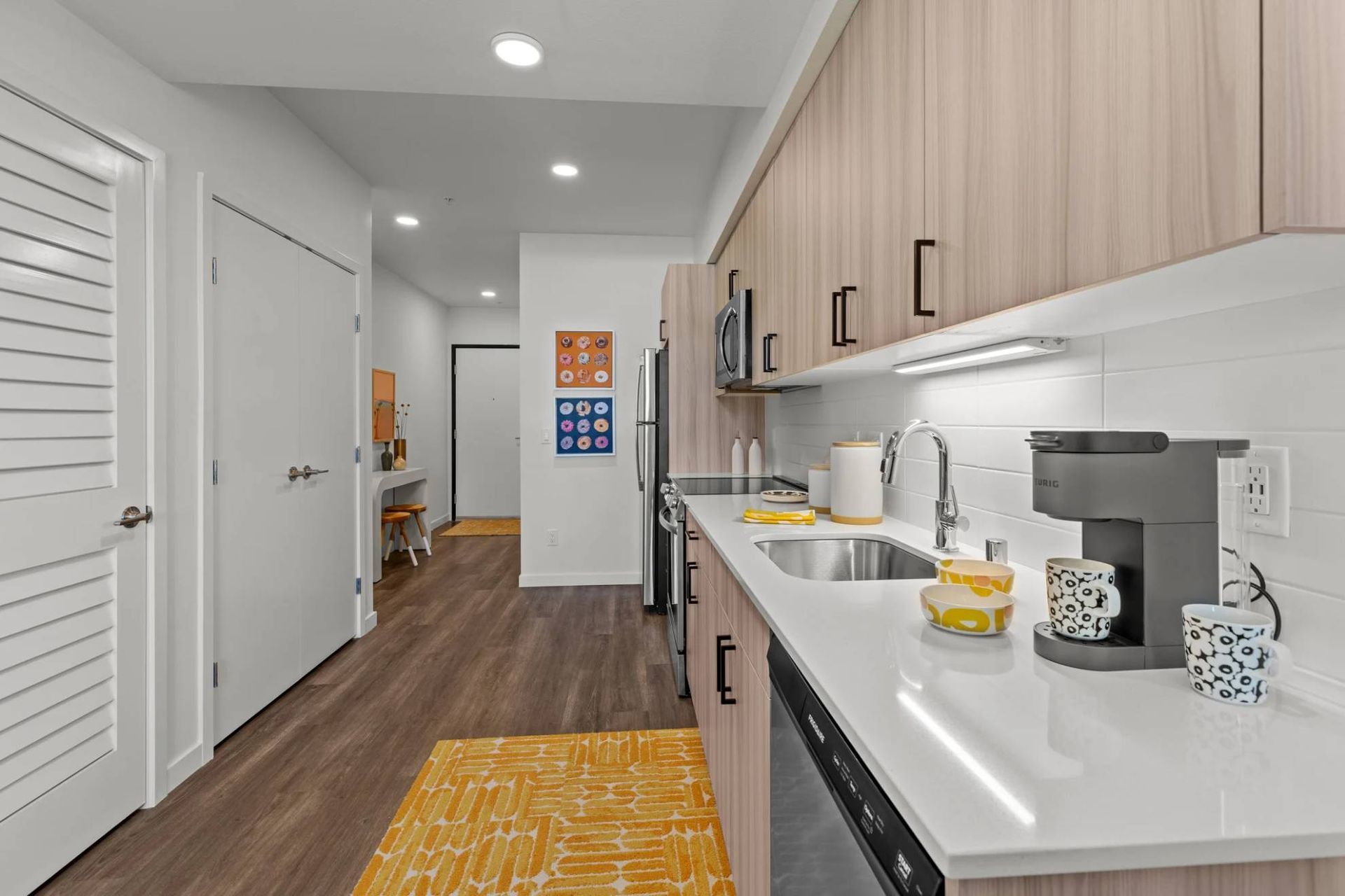 Bright, modern apartment kitchen with wood-tone cabinets, white countertops, and stainless appliances at Zinnia Apartments in Shoreline, WA.