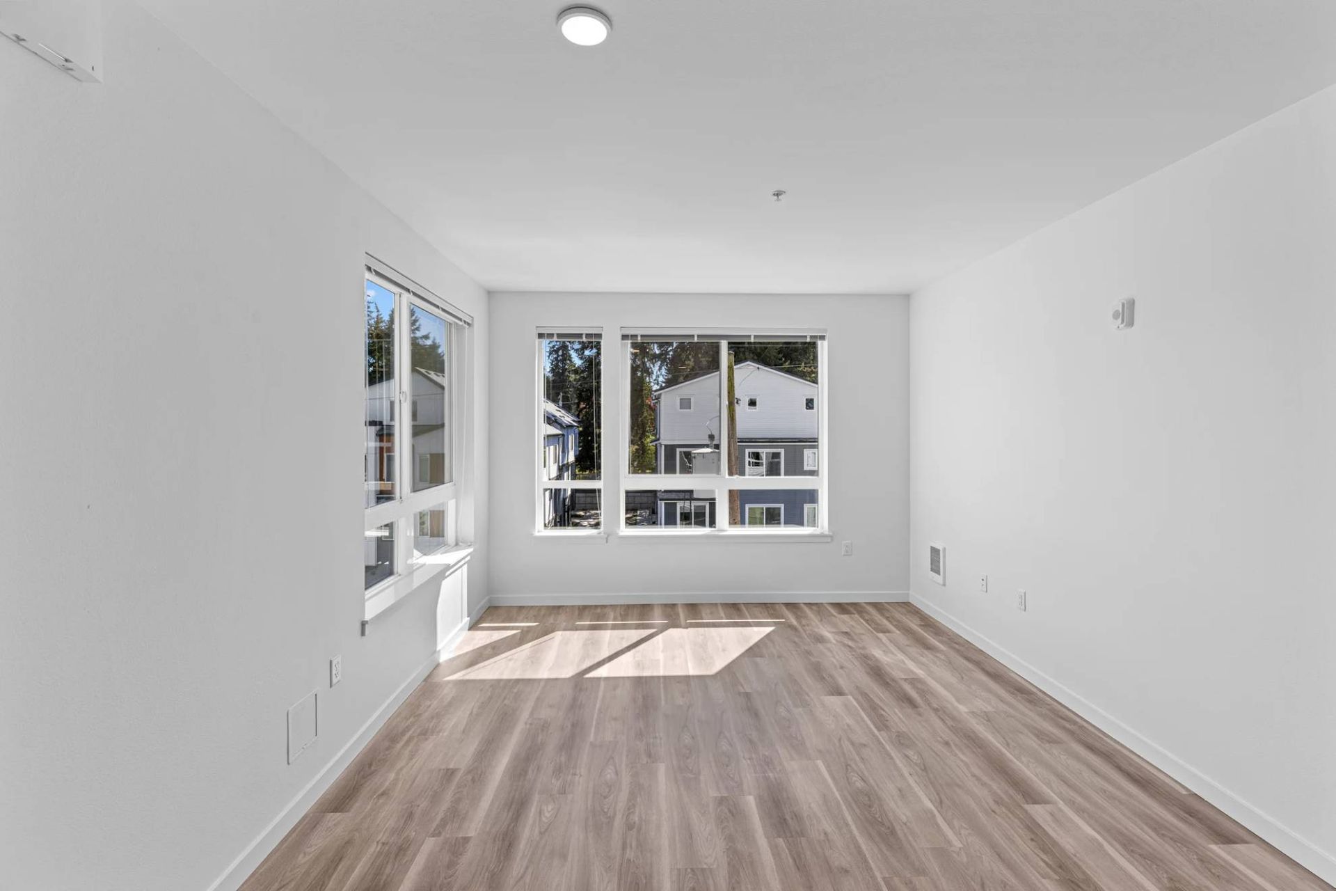 Bright empty living room with large windows and wood-look flooring at Zinnia Apartments in Shoreline, WA.