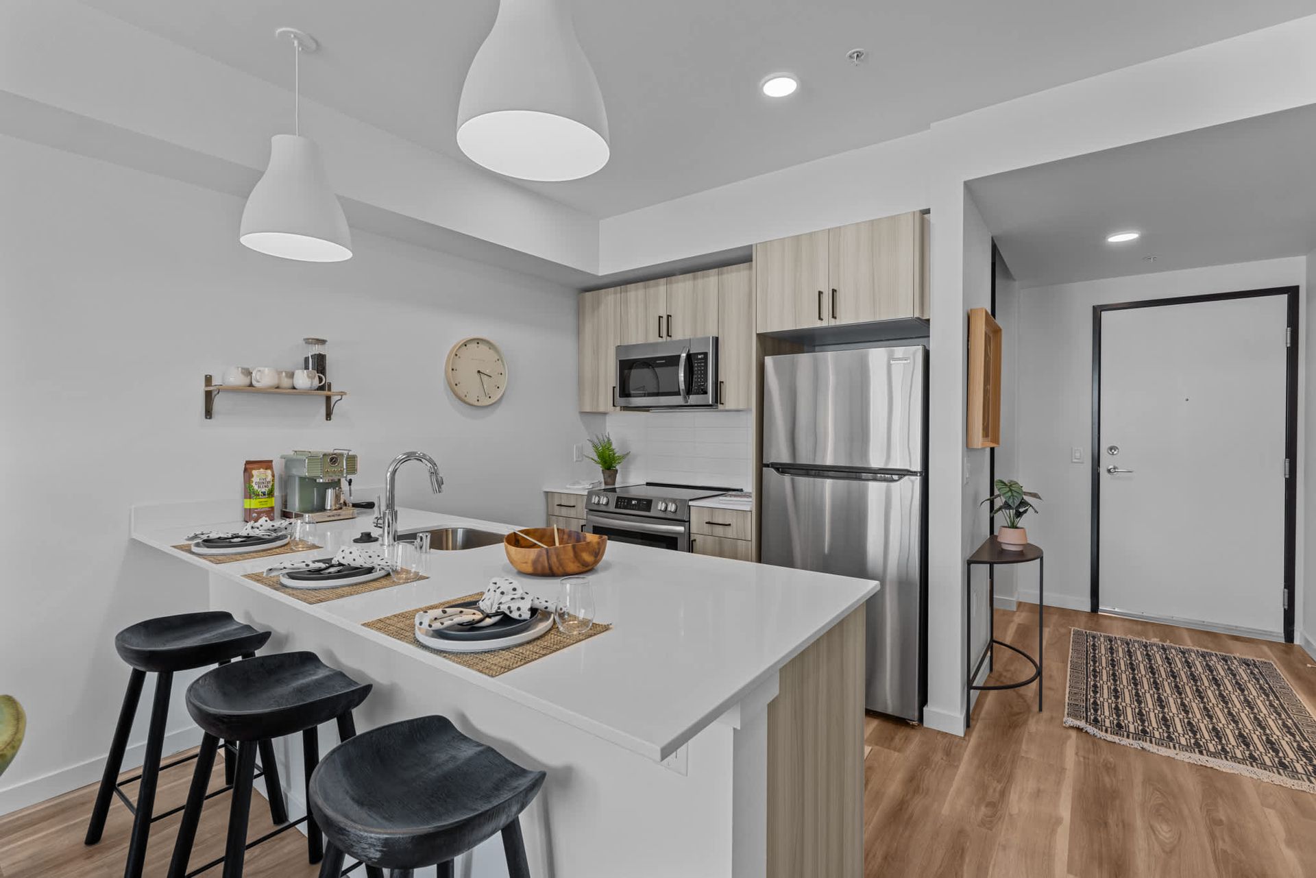 Modern apartment kitchen with island, three black bar stools, and stainless steel appliances at Zinnia Apartments in Shoreline, WA.