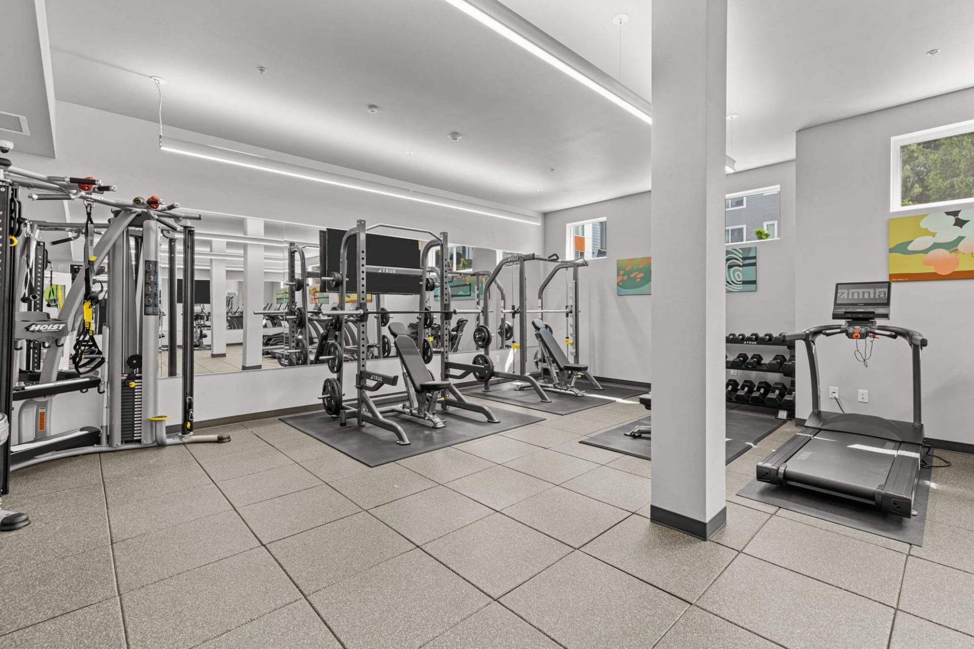 Interior of a modern communal gym with weight machines, benches, and a treadmill at Zinnia Apartments in Shoreline, WA.