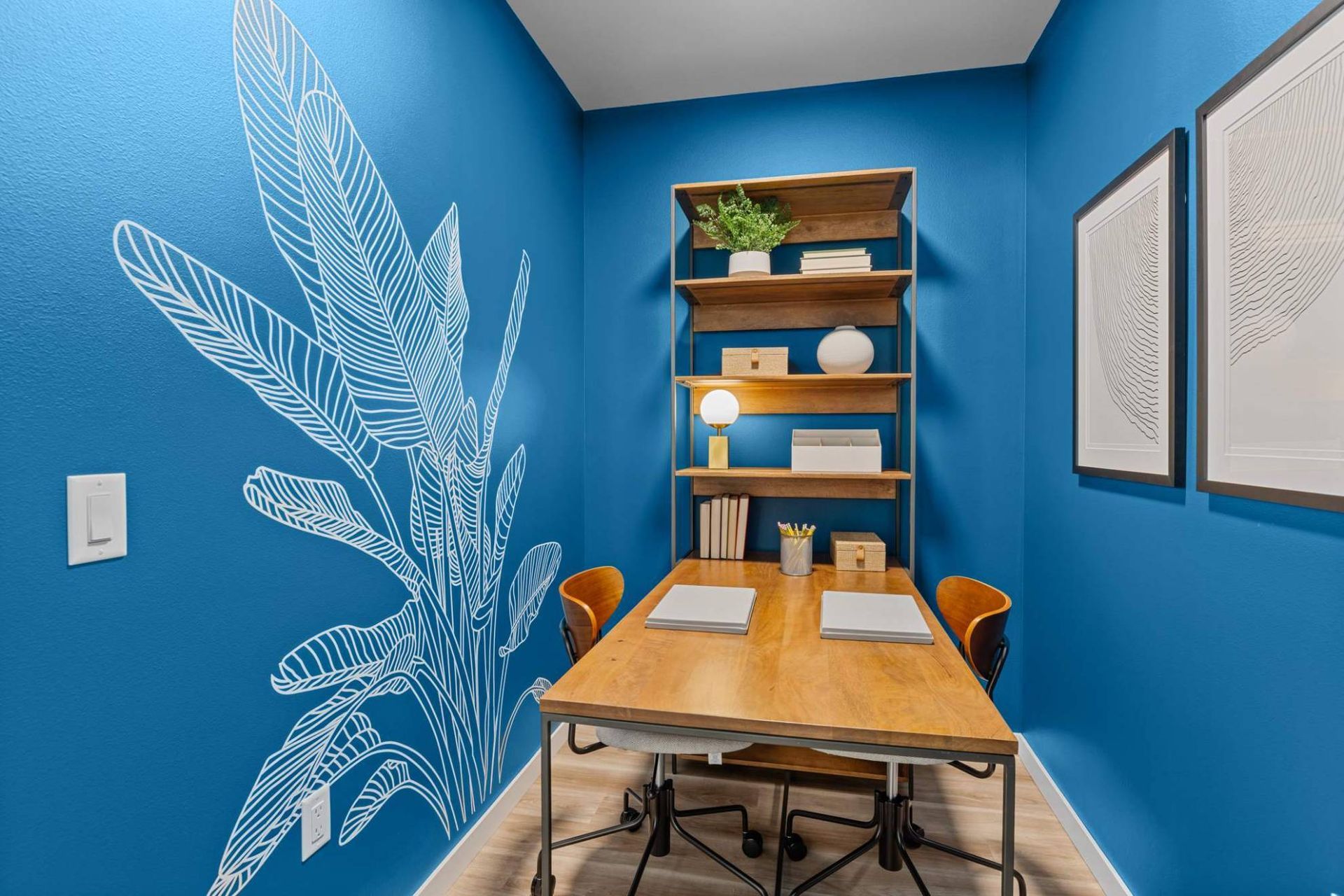 Blue-painted study nook with a wooden desk, two chairs, and shelving unit at Zinnia Apartments in Shoreline, WA.