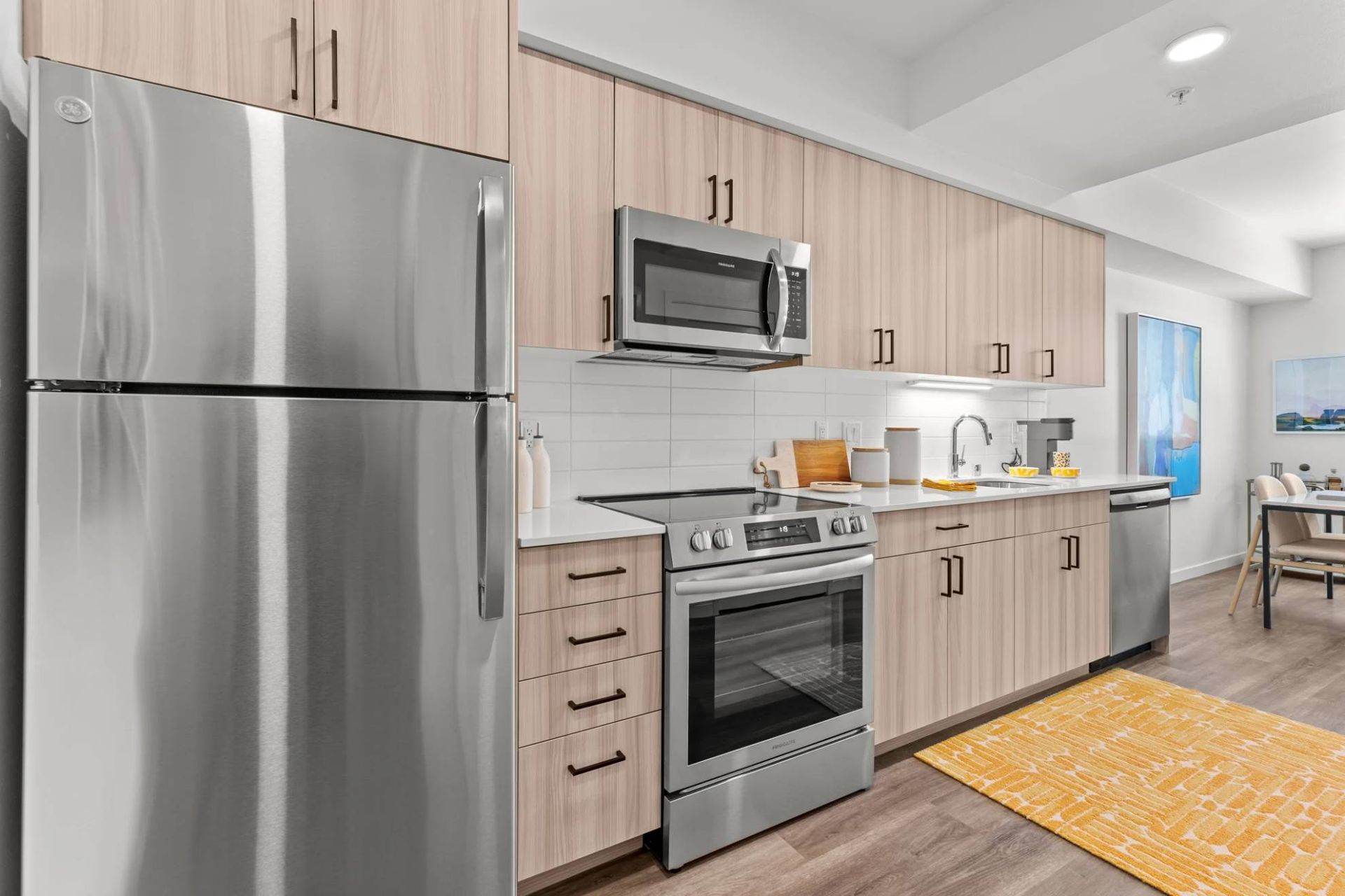 Modern kitchen in an apartment with stainless steel fridge, oven, microwave, and light wood cabinets at Zinnia Apartments in Shoreline, WA.