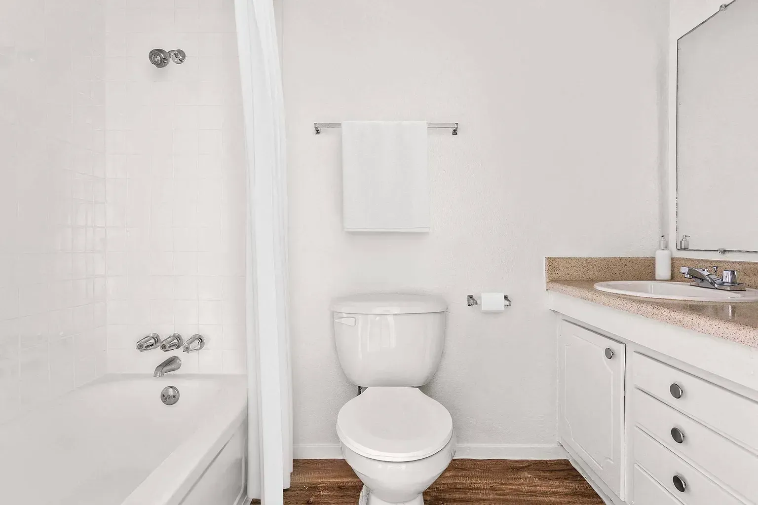 White bathroom featuring a toilet, vanity with sink, shower curtain, and towel rack.
