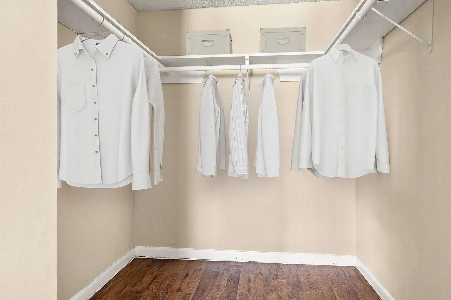 Walk-in closet with white shirts hanging on a rod; beige walls and wooden floor.