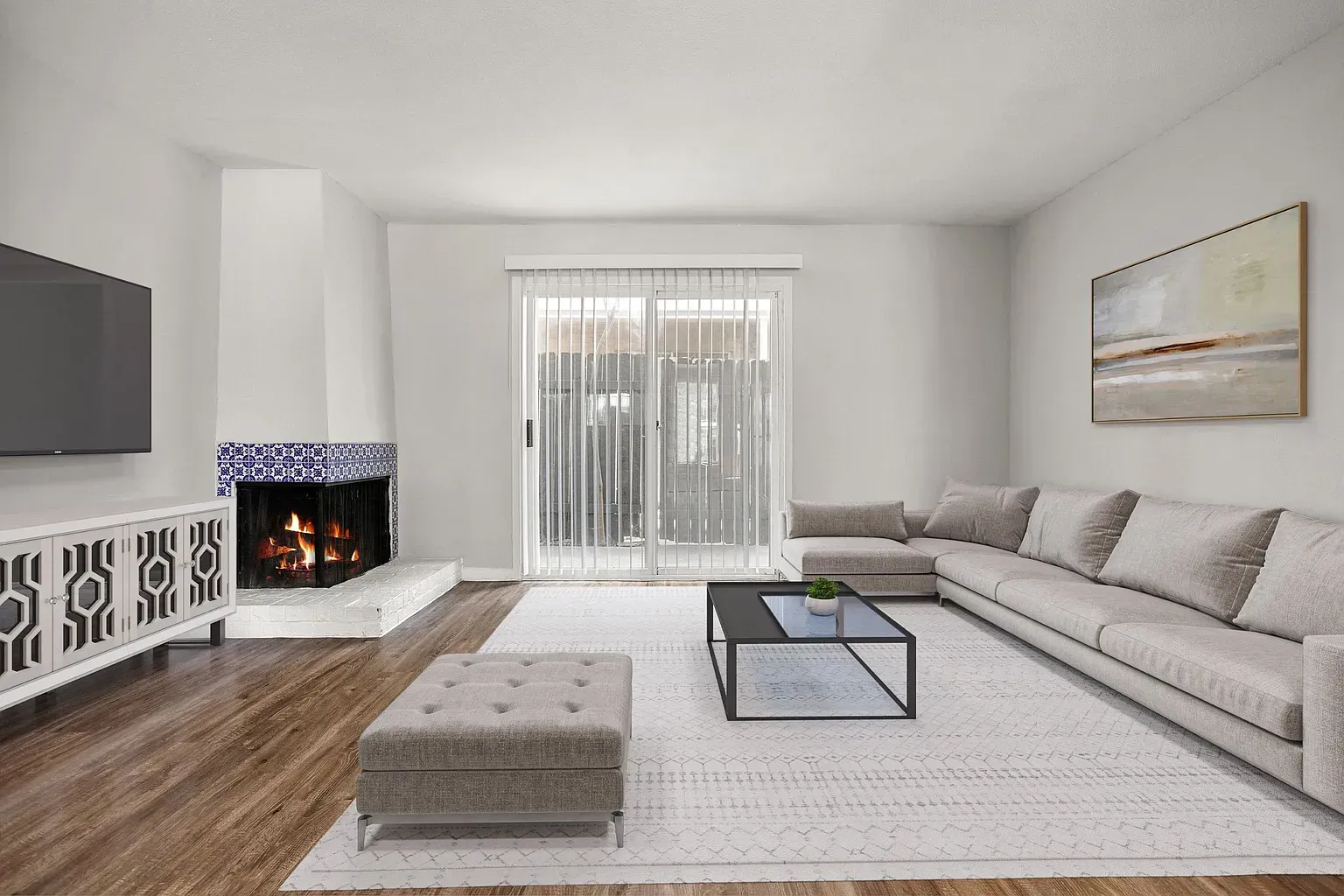 Living room in an apartment with a beige sectional, fireplace, TV, and sliding glass door.