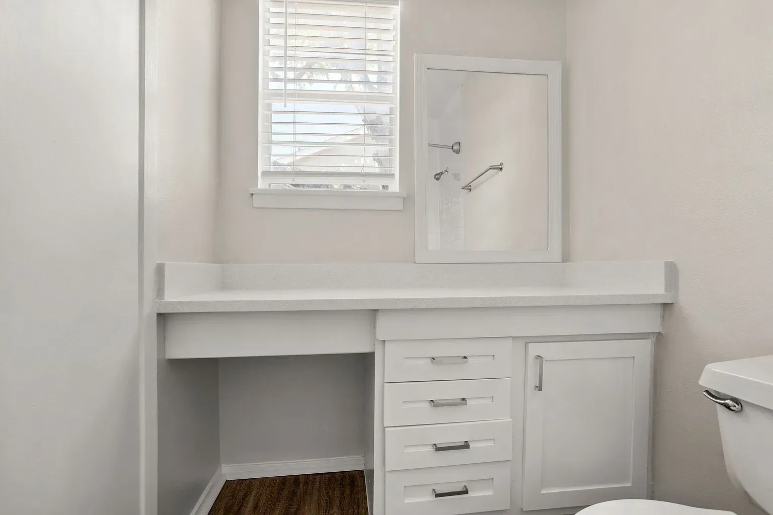 Bright bathroom with white vanity, countertop, mirror, window blinds, and cabinet storage.