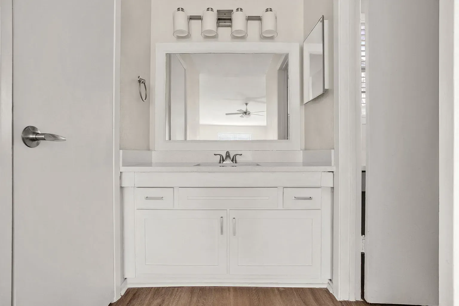 White bathroom vanity with sink, mirror, and a four-light fixture in an apartment.
