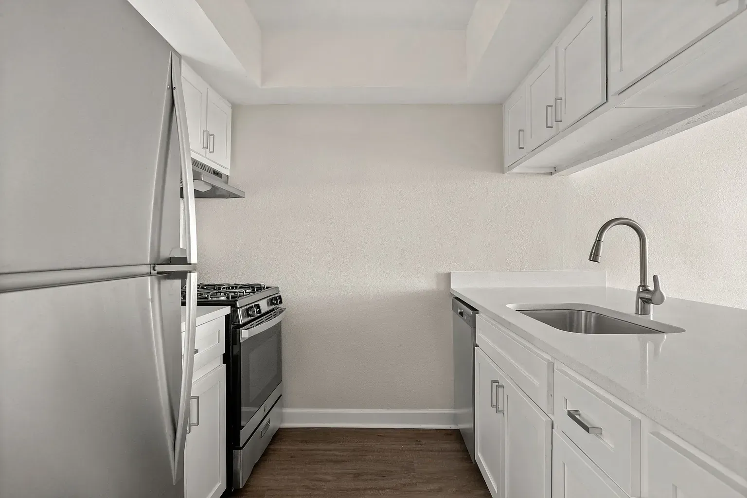 Compact white kitchen with upper cabinets, stainless steel fridge, stove, and a sink.