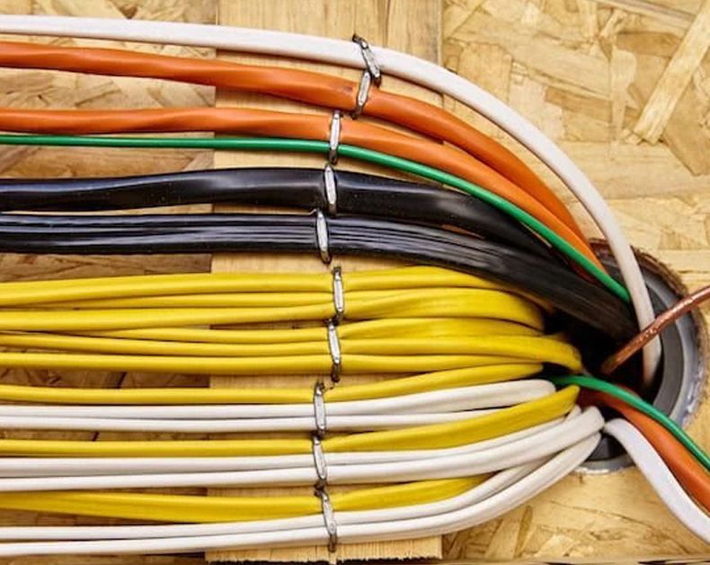 A bunch of wires are coming out of a hole in the wall