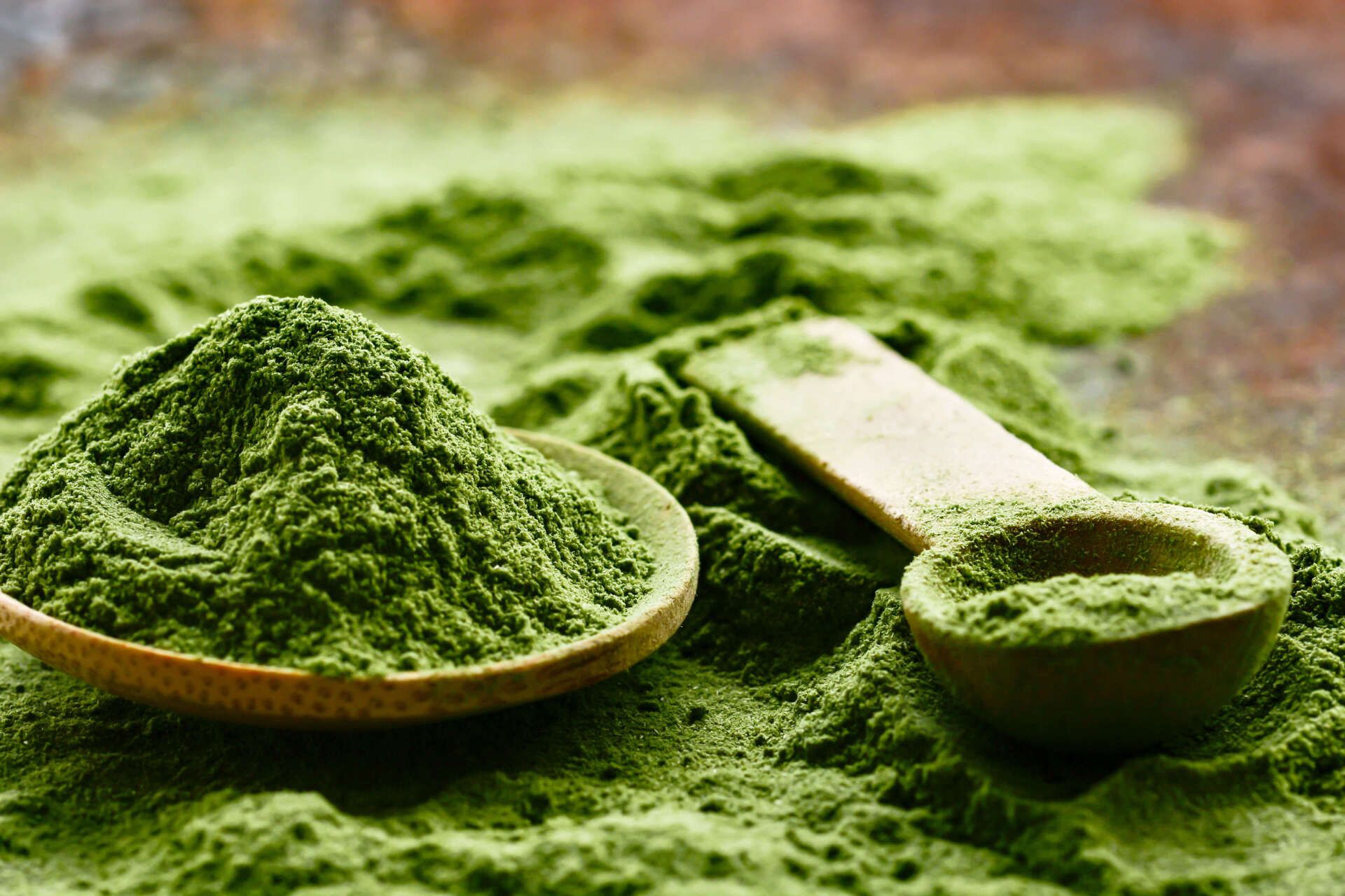 A wooden spoon filled with green powder is sitting on top of a pile of green powder.