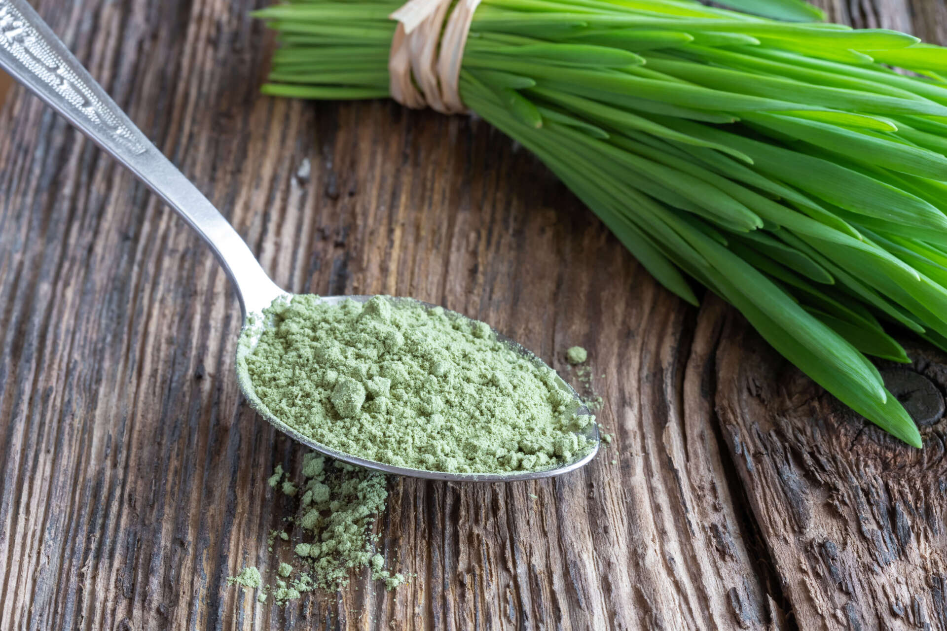 A spoon filled with green powder next to a bunch of green onions on a wooden table.