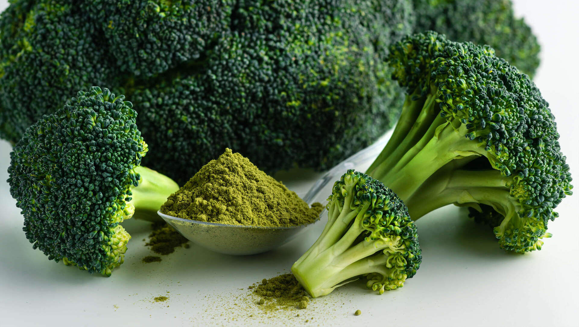 Broccoli and a spoon of broccoli powder on a table.
