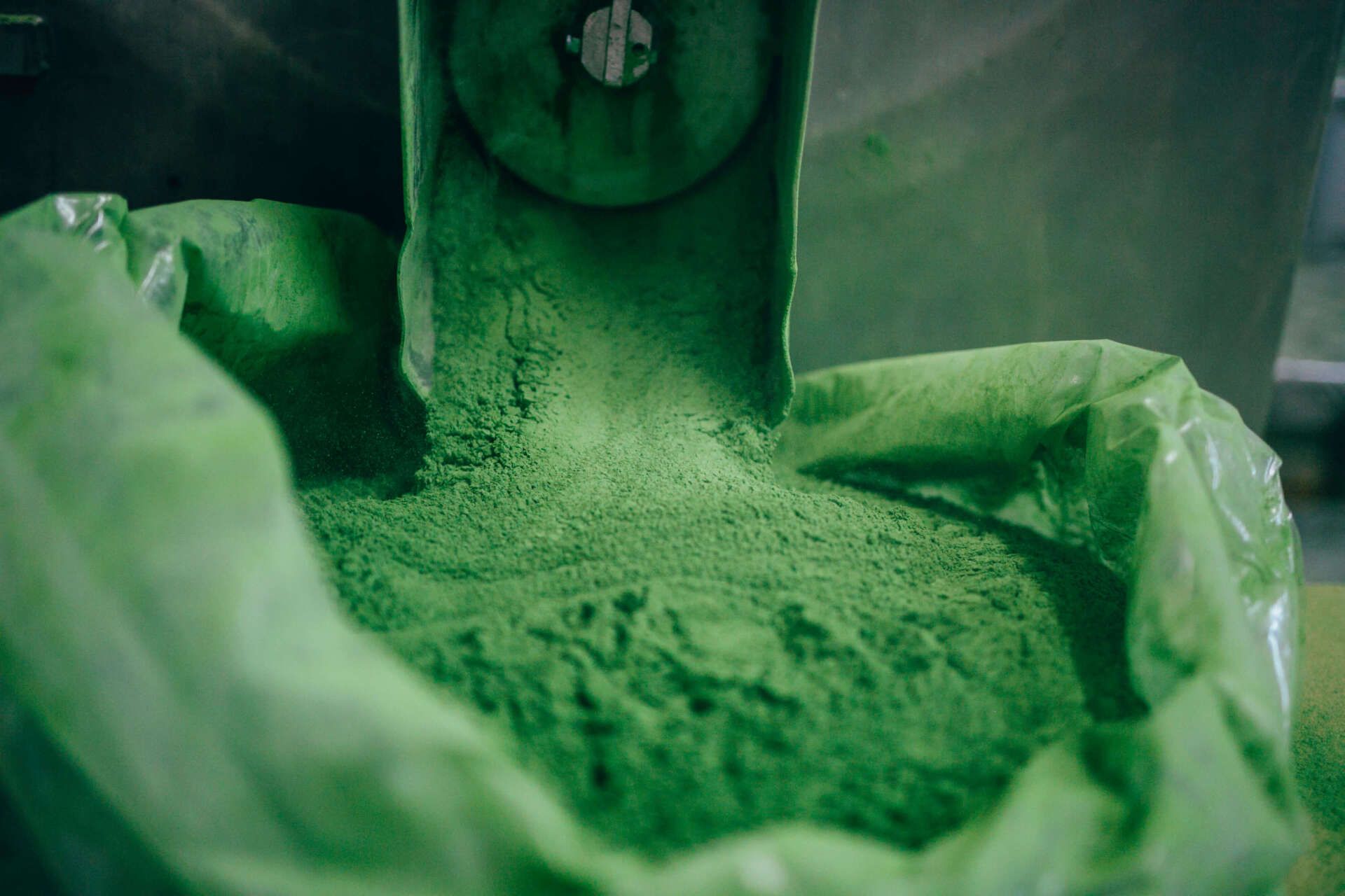 A bag of green powder is being poured into a machine.