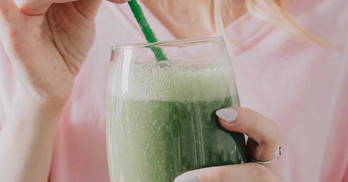A woman is drinking a green smoothie with a green straw.