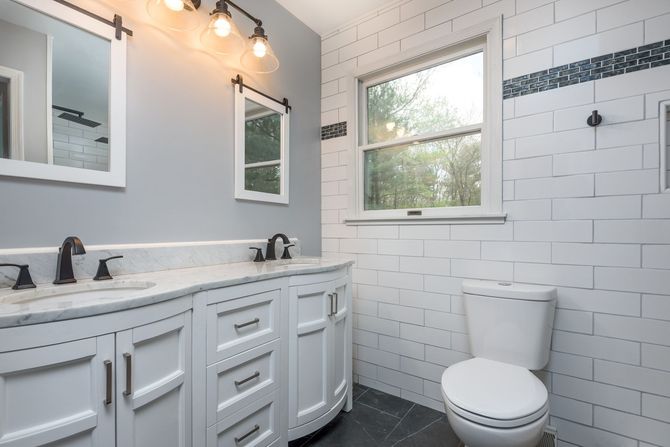 A bathroom with a toilet , sink , mirror and window.