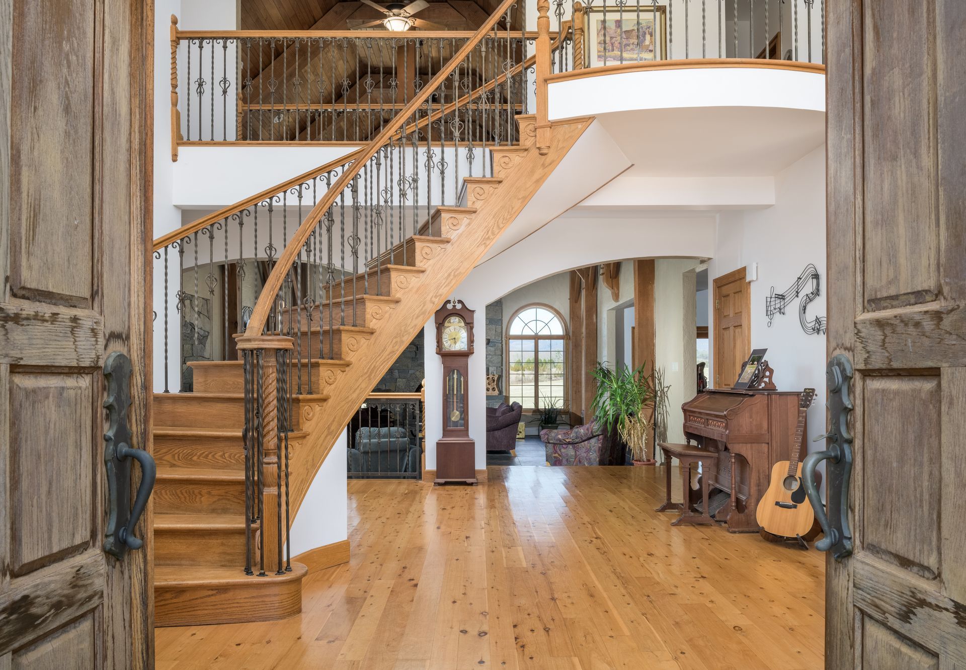 A wooden staircase in a house with a grandfather clock and a piano.