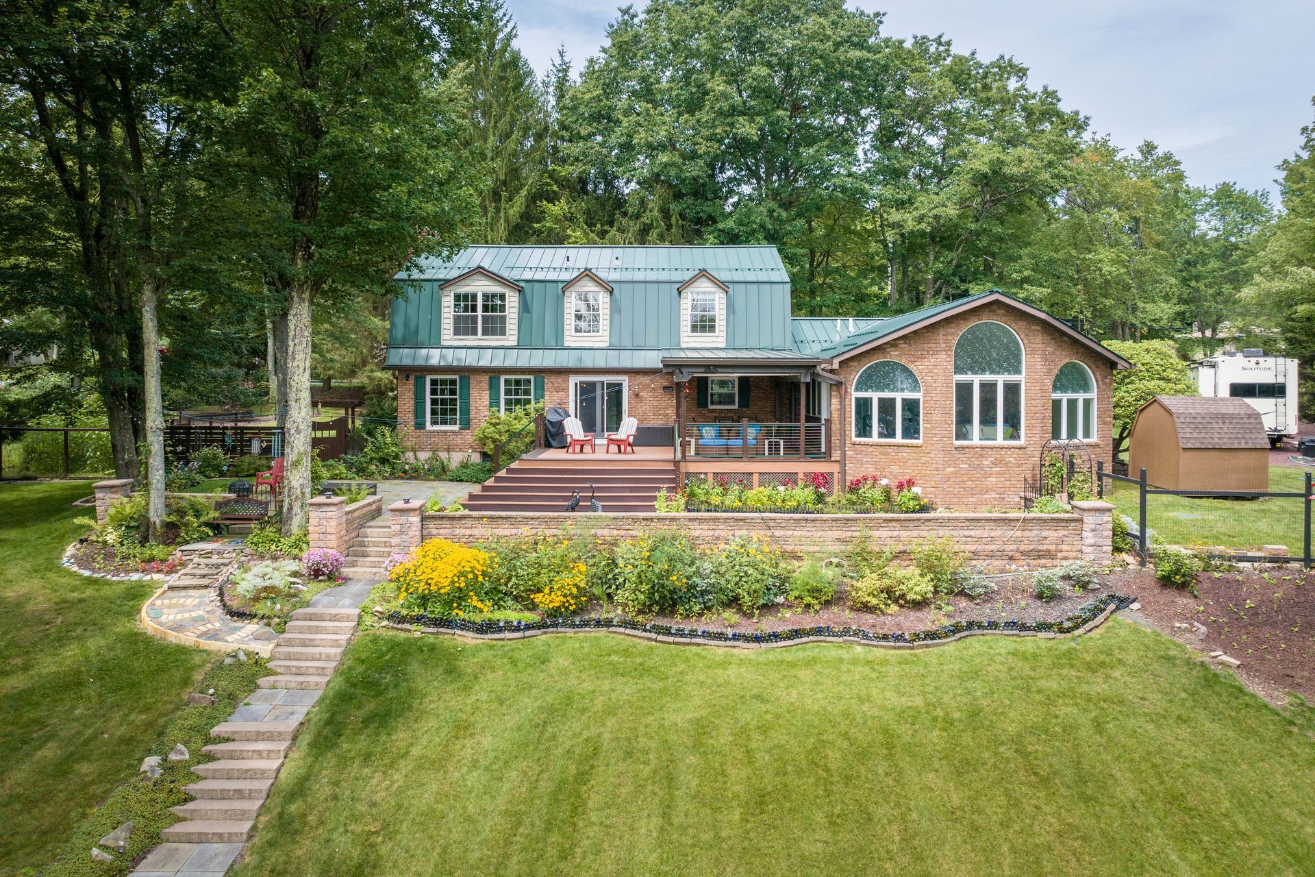 A large brick house with a green roof is surrounded by trees and grass.