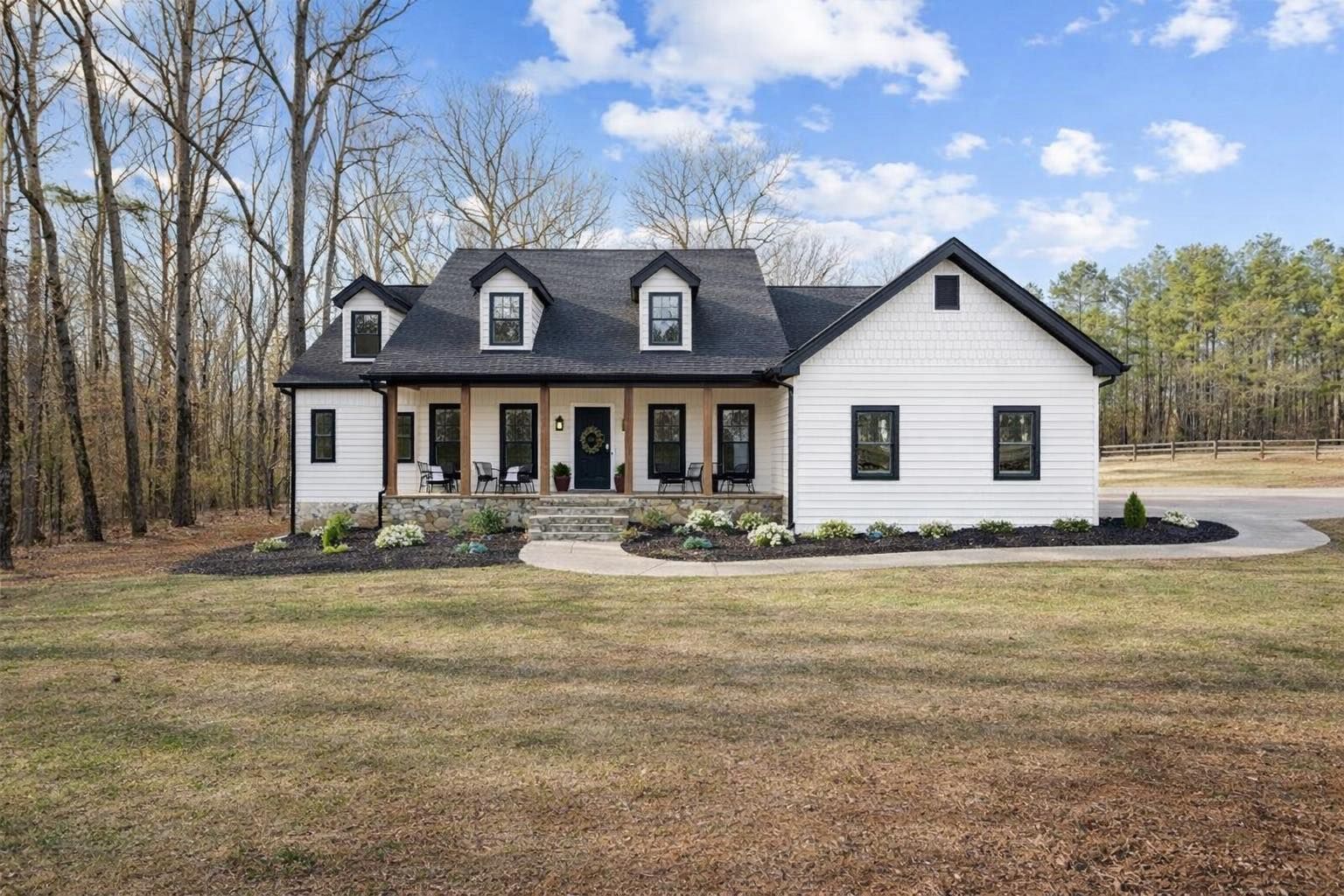 White house with black trim, three dormers, and a small front porch, in a grassy setting.
