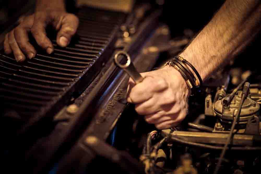 close up of someone holding a wrench under the hood of a car