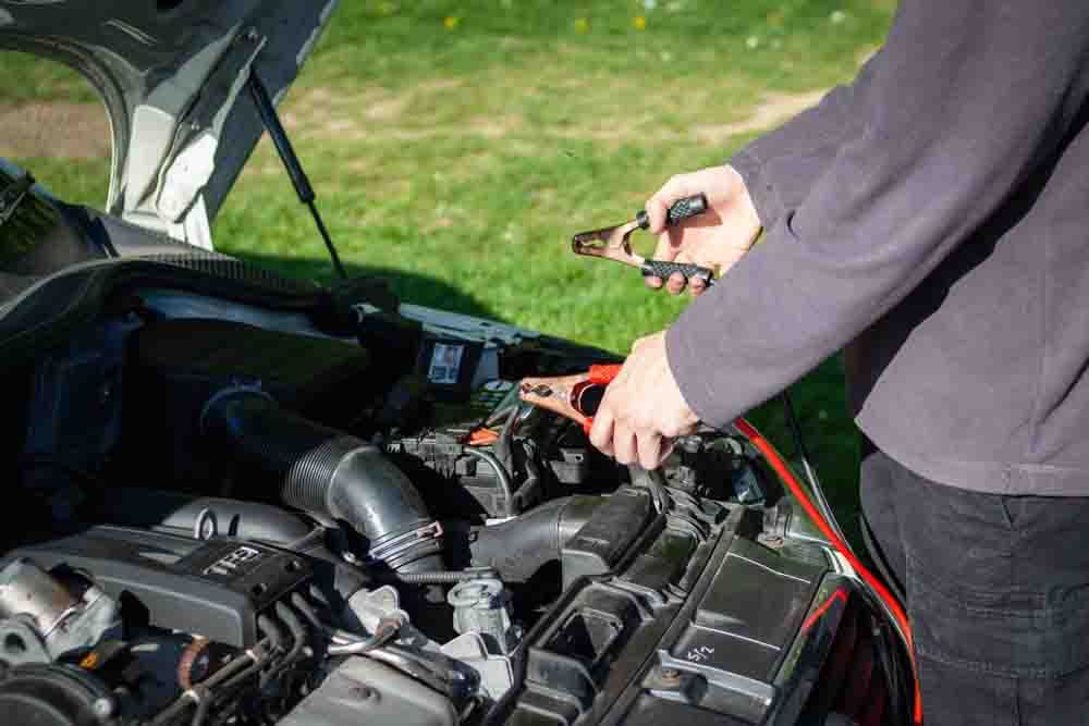 mechanic hooking up jumper cables to the car battery
