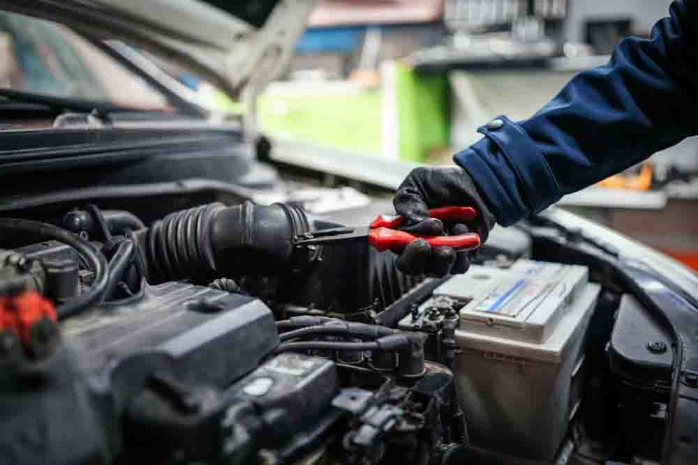 close up of an engine bay with a mechanics hand holding pliers