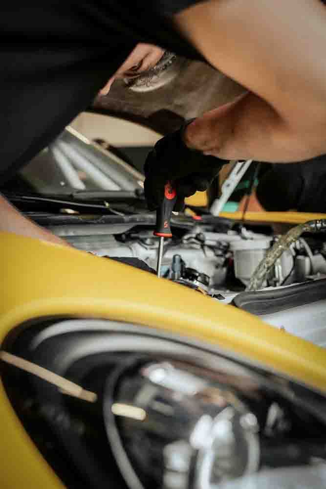 a mechanic looking under the hood of a car and using a screwdriver