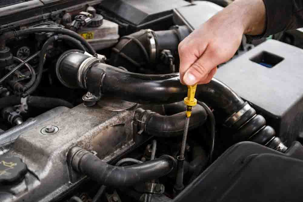 a hand pulling out the oil dipstick under the hood of a car