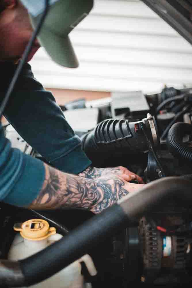 a mechanic with a green hat performing work under the hood of a car