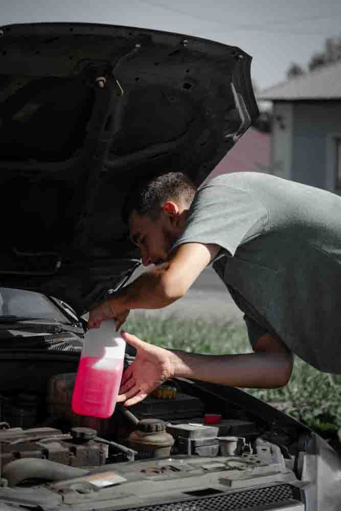 mechanic pouring in a pink coolant liquid into the engine of a car