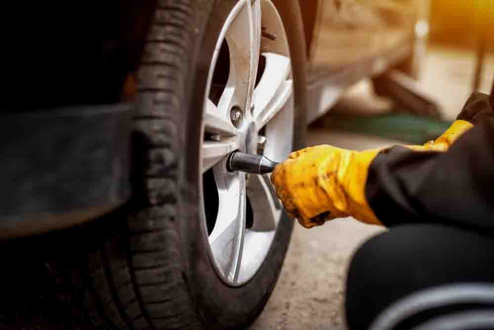 close up of a car wheel being secured by a mechanic with yellow gloves