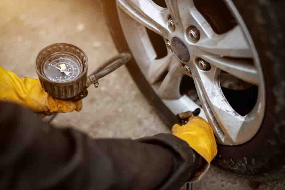 close up of mechanic with yellow gloves adjusting the tire pressure of a wheel with a guage