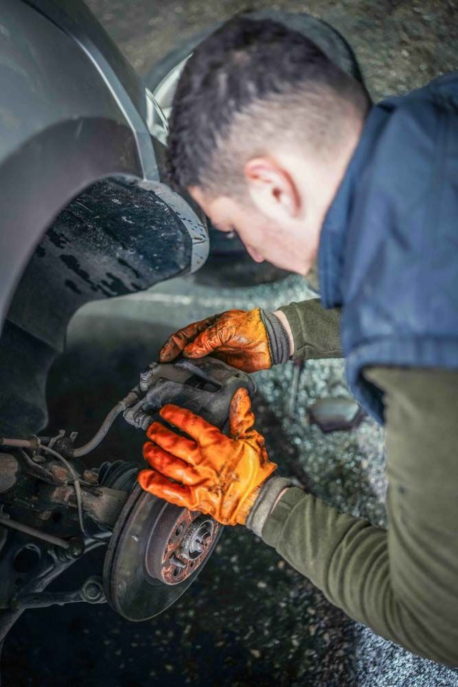 A mobile mechanic in Barrie working on a brake calliper and brake pads in orange gloves