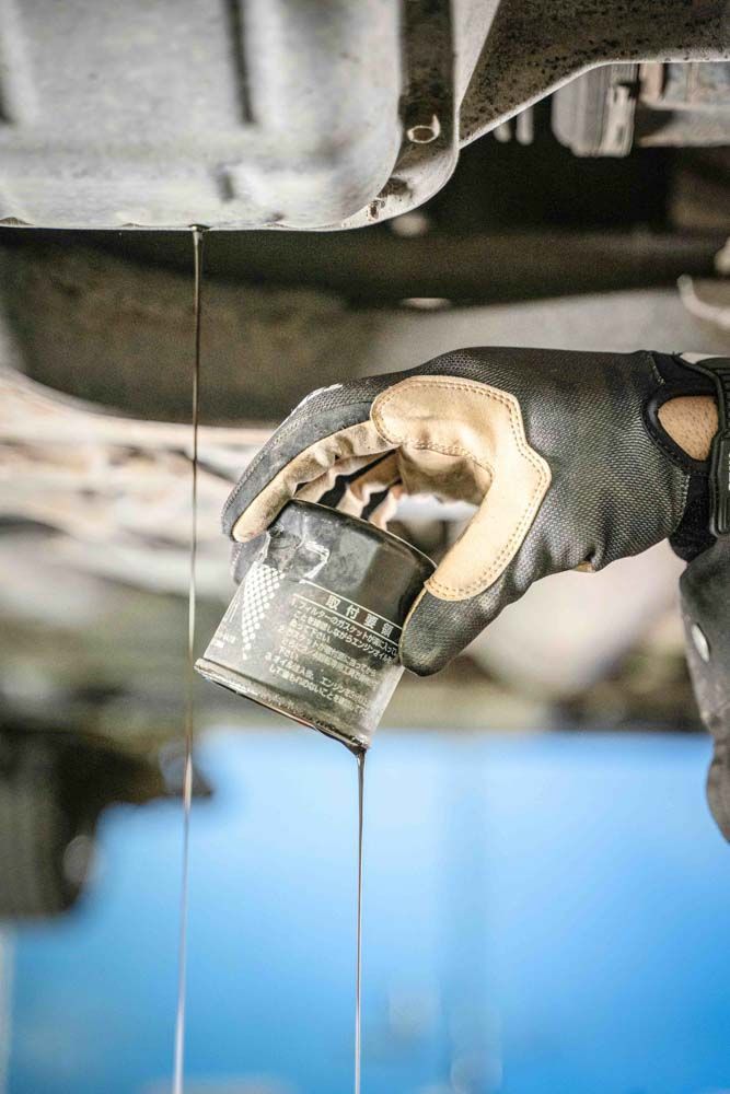 a close up of a oil filter being held by a mechanics hand with gloves while engine oil drips out doing an oil change
