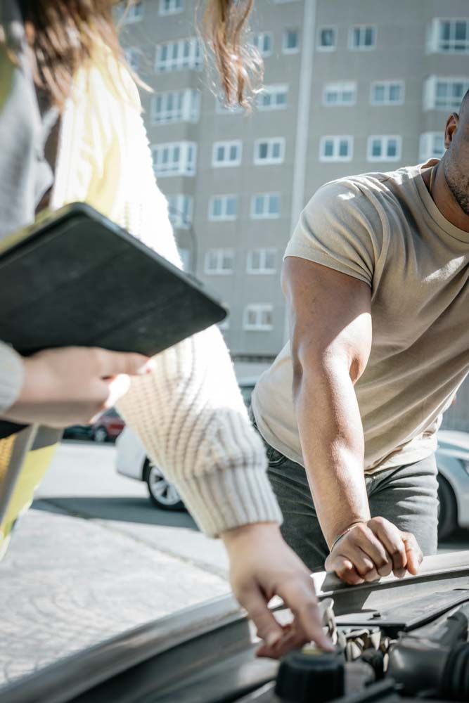 A girl inspecting under the hood of a used car with a clipboard