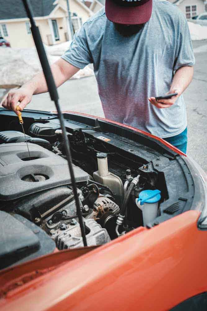 A Barrie mobile mechanic is looking under the hood of an orange used car and checking the state of the engine oil during a pre-purchase inspection