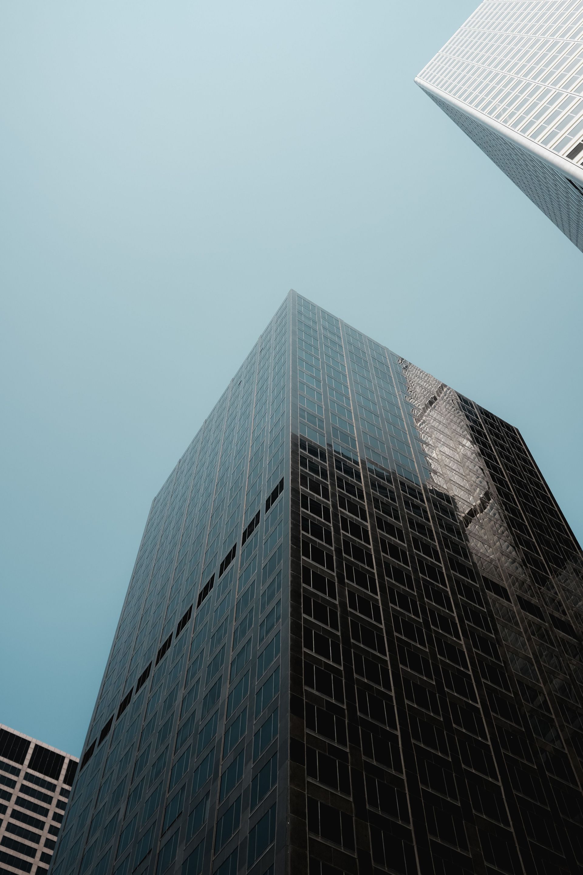 Tall dark glass skyscrapers seen from below against a pale blue sky
