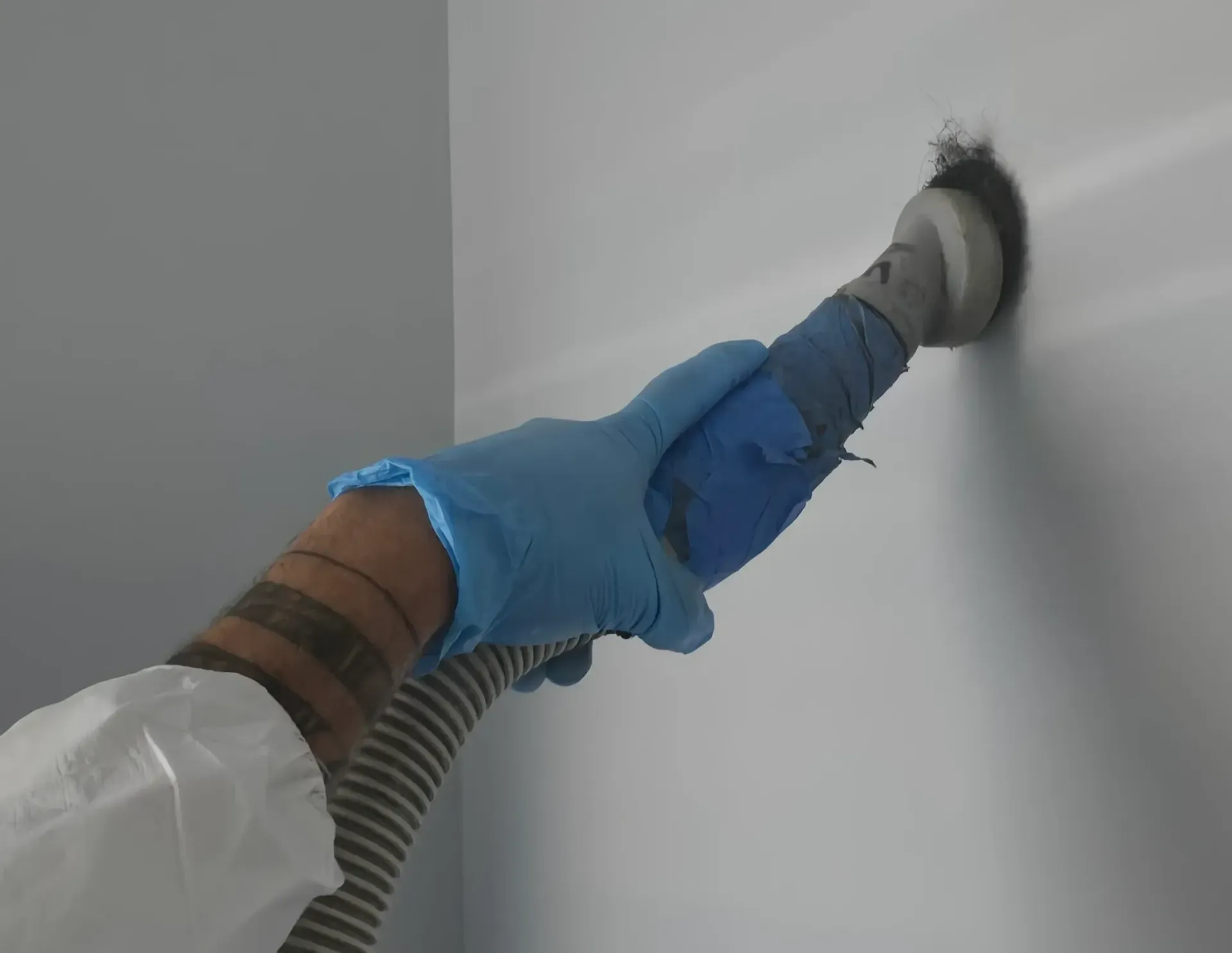 A person wearing blue gloves is using a vacuum cleaner on a wall.