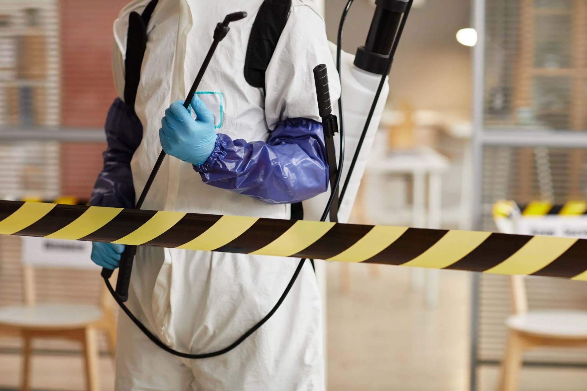 A man in a protective suit is spraying a room with a sprayer.