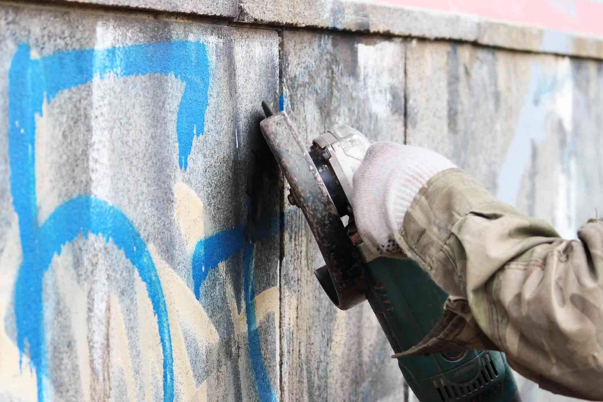 A person is using a grinder to remove graffiti from a wall.