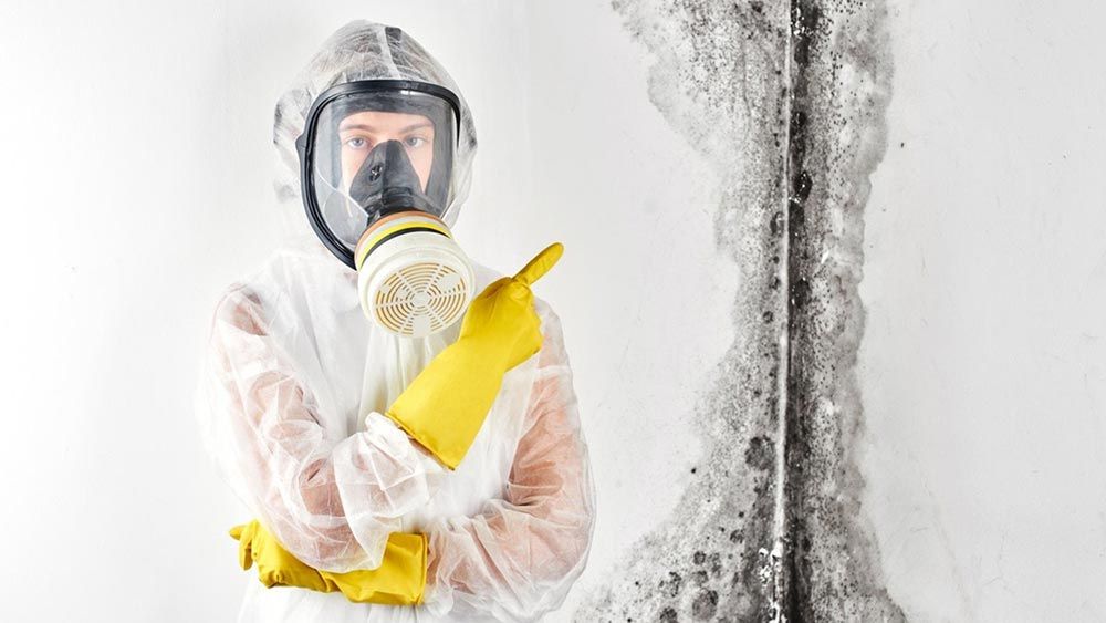 A person wearing a gas mask and gloves is standing in front of a wall.