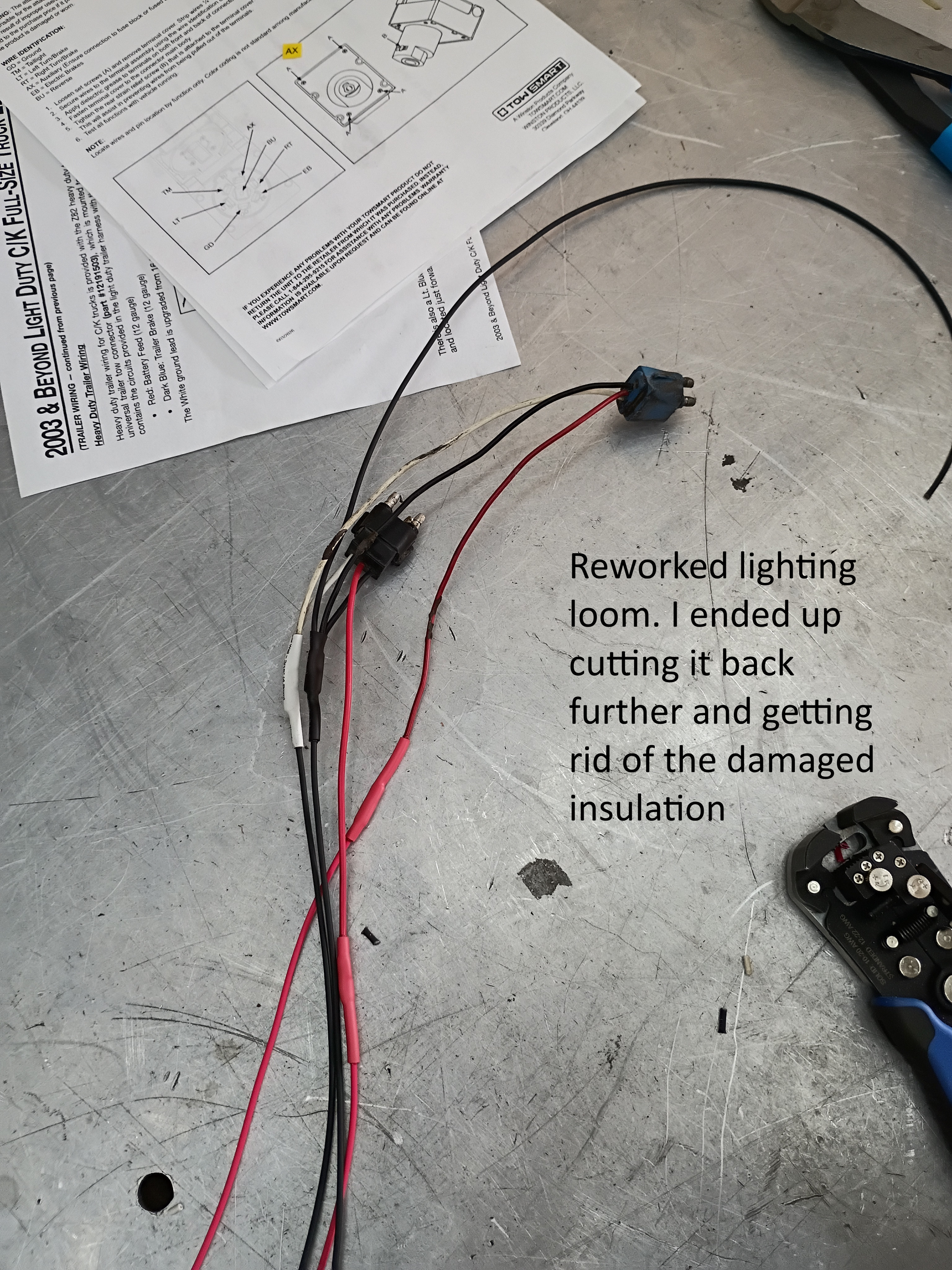 Damaged red and black wires on a concrete floor with repair notes and a tool partially visible