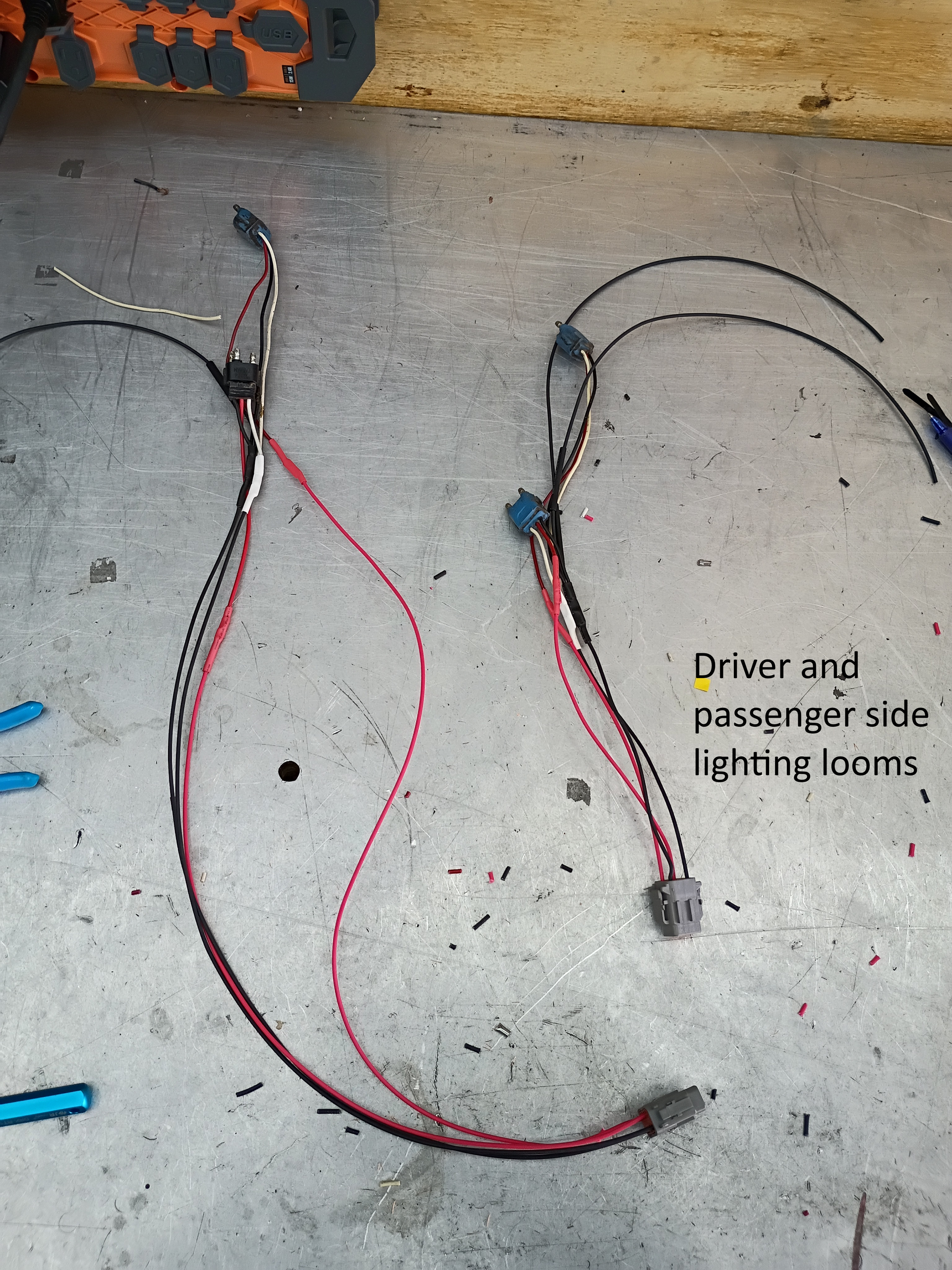 Two red and black wiring harnesses on a concrete floor, labeled for driver and passenger side tail lights
