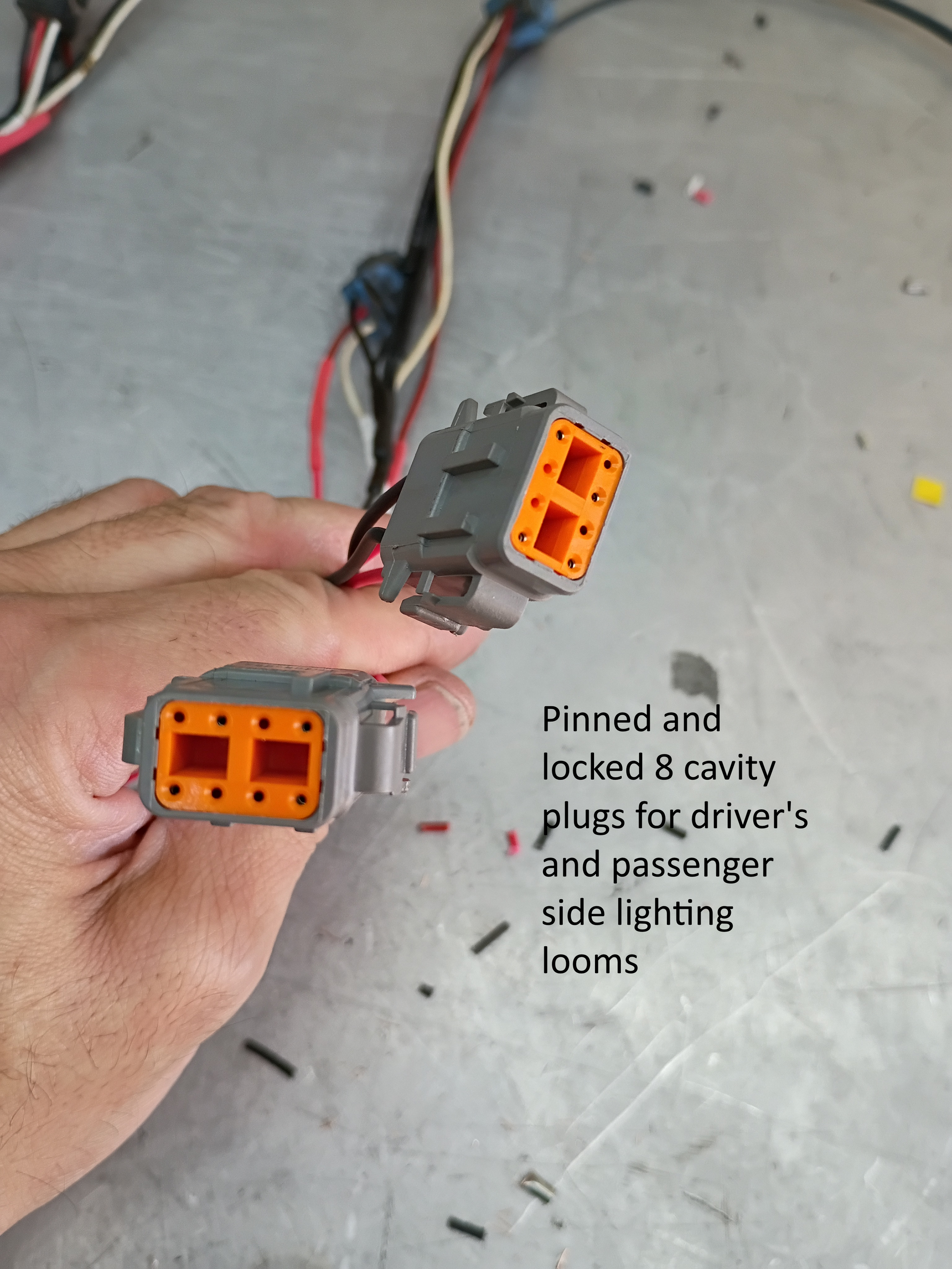 Hands holding two orange electrical connectors with wires on a gray surface, near a caption about pinned and locked plugs.