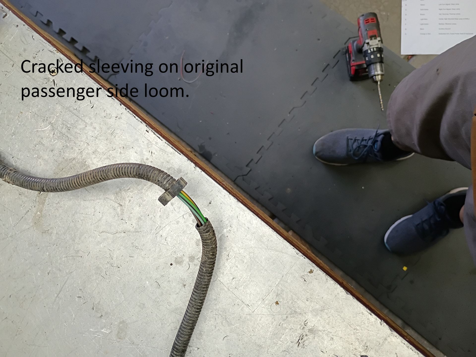 Cracked black loom cable on a floor beside a person’s shoe and a red tool on a mat