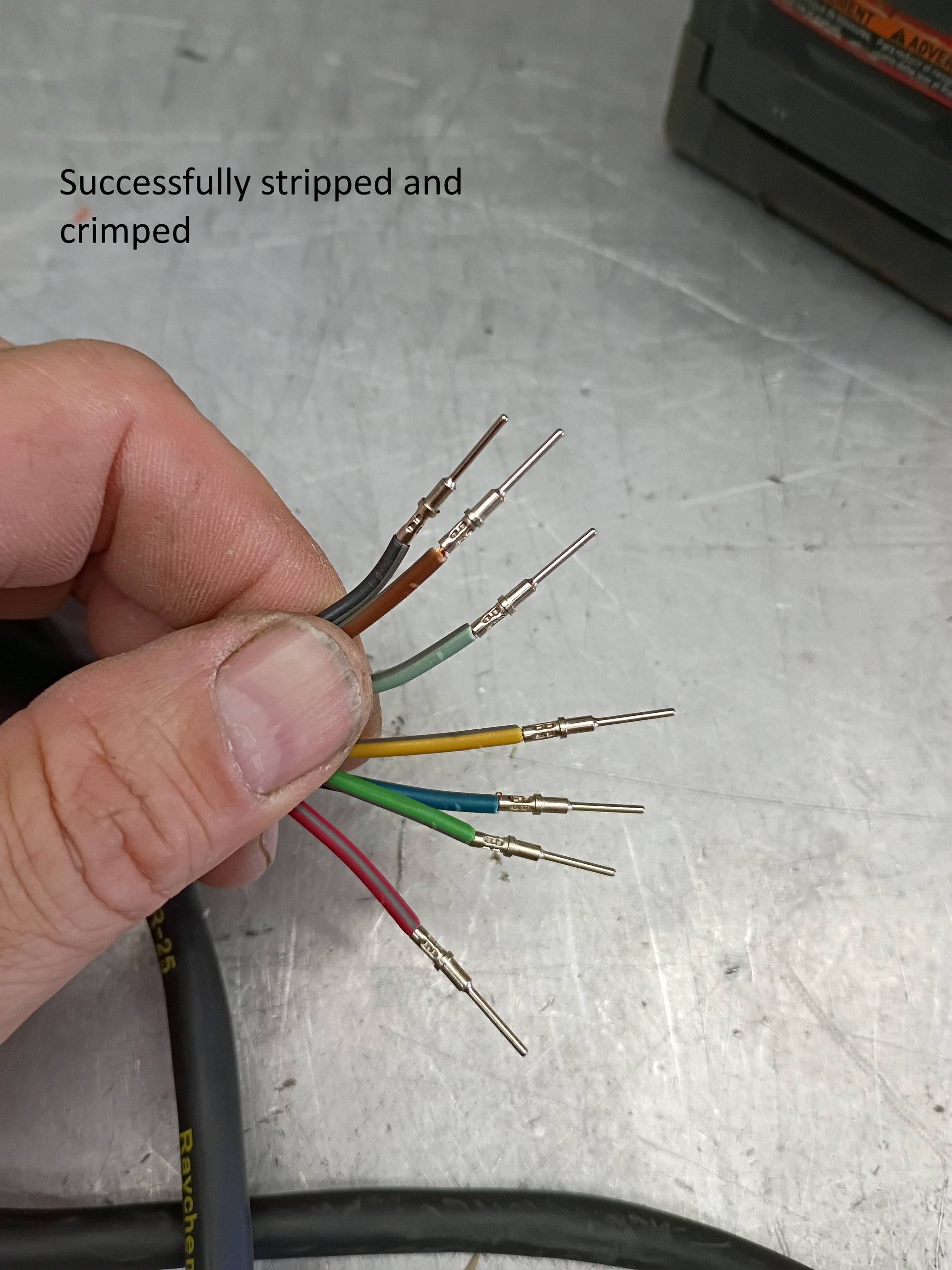 Hand holding stripped multicolored cable wires on a metal workbench