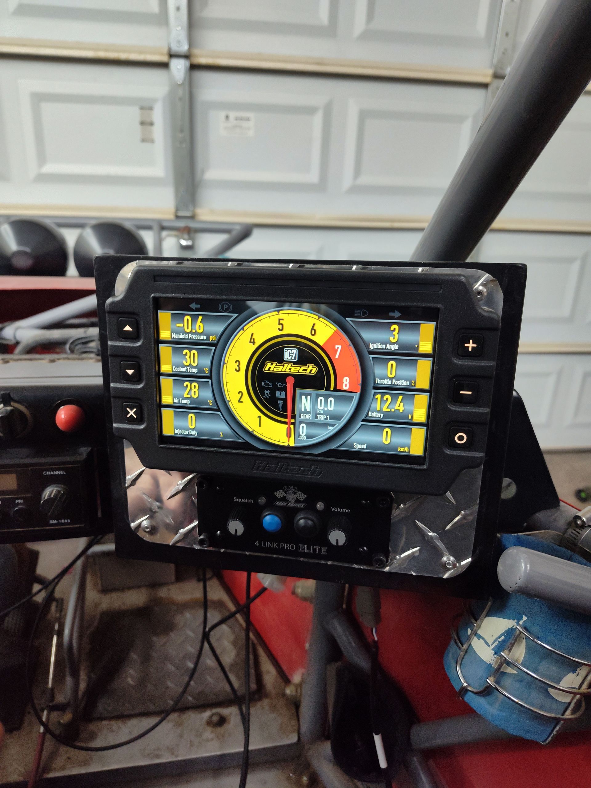 Car dashboard-mounted touchscreen showing a colorful gauge-style interface in a garage.