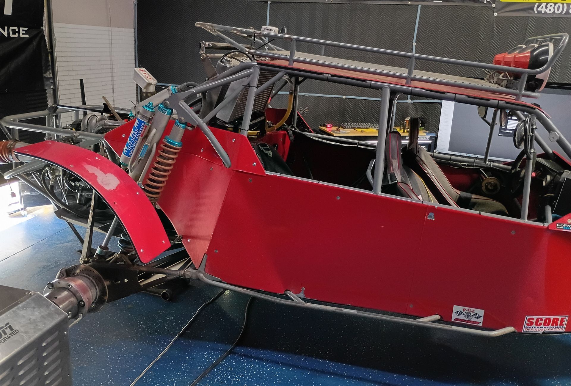 Red off-road buggy with exposed roll cage and large rear tire on a platform indoors