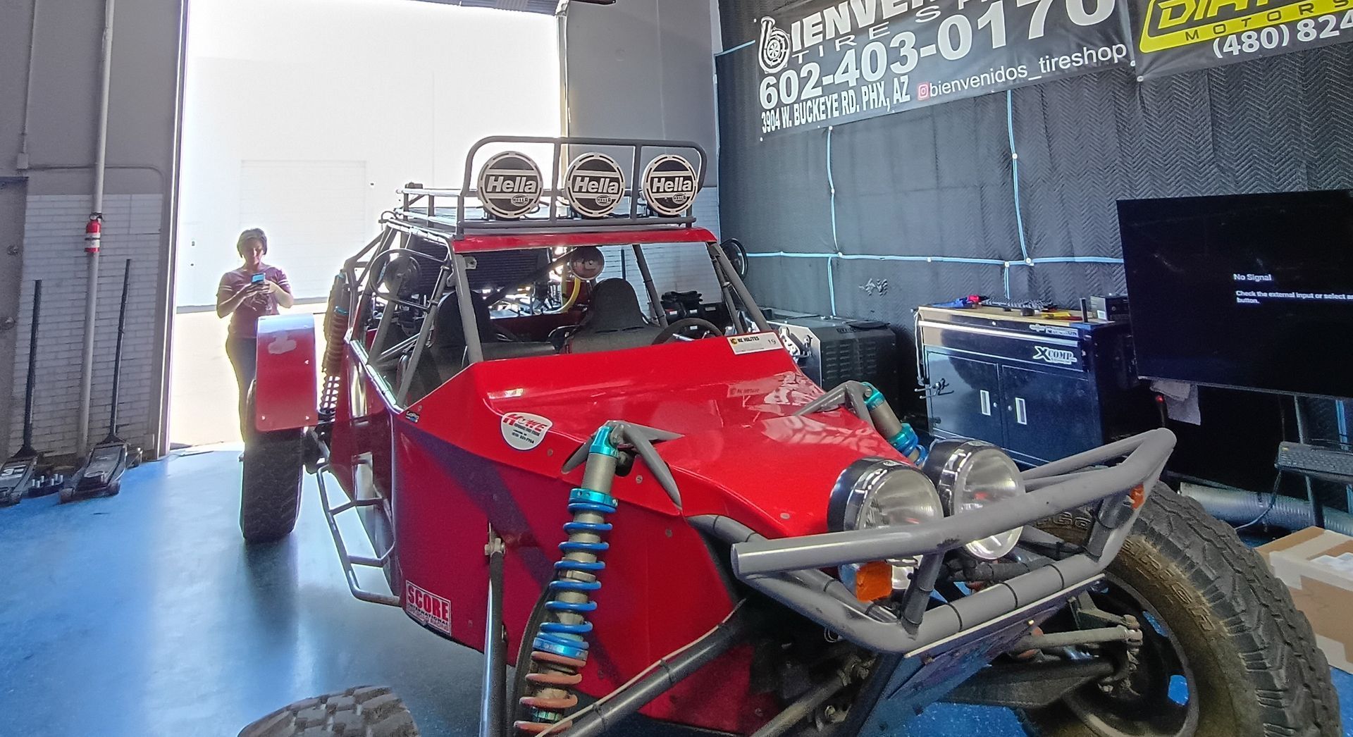 Red off-road buggy in a garage, with a person standing beside it and a TV screen on the right.