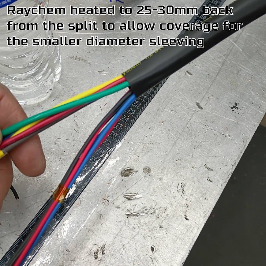 Hands holding multicolored wires with black heat-shrink tubing on a metal workbench.